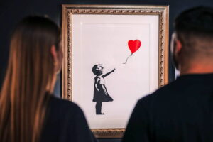Banksy - Mädchen mit Ballon (Girl with Balloon): Ikonisches Street-Art-Motiv in einem Goldrahmen, betrachtet von Museumsbesuchern