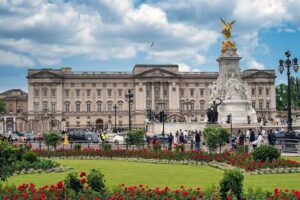Buckingham Palace - London - Außenansicht: Der imposante, symmetrische Haupteingang mit wehender Flagge des Monarchen und dem Victoria Memorial im Vordergrund