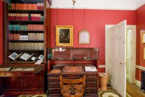 Charles Dickens Museum - London - Arbeitszimmer: Innenraumansicht des Zimmers mit dem historischen Schreibtisch, der Bibliothek und Porträts an den roten Wänden