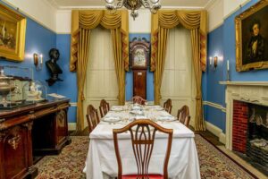 Charles Dickens Museum - London - Esszimmer: Das historische Zimmer mit gedecktem Tisch, blauen Wänden, Gemälden und einer antiken Standuh