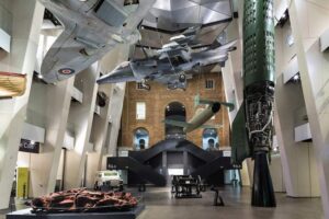 Imperial War Museum London - Ausstellung: Das Atrium mit ikonischen Exponaten, darunter die hängenden Flugzeuge wie Spitfire und Harrier sowie ein Segment der V-2 Rakete