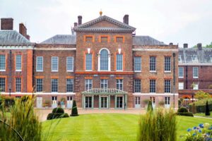 Kensington Palace - London - Außenansicht: Ein herrschaftliches Backsteingebäude mit symmetrischer Fassade vor einer gepflegten Rasenfläche mit dekorativen Hecken