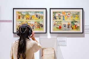 Museum am Rothenbaum - Hamburg - Ausstellung - Druckfrisch aus den Zwanzigern: Eine Besucherin betrachtet zwei gerahmte Bilder mit asiatischen Illustrationen an einer weißen Wand