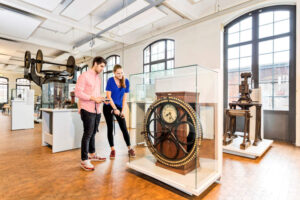 Museum der Arbeit - Hamburg - Arbeiterkontrolluhr: Besucher betrachten eine historische Kontrolluhr aus dem Industriezeitalter