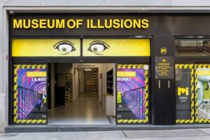 Museum of Illusions Madrid - Außenansicht: Frontale Aufnahme des Eingangsbereichs des Museums mit dem gelb-schwarzen Logo