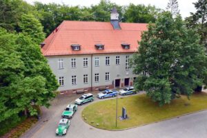 Polizeimuseum Hamburg: Das Museumsgebäude mit einer Schlange historischer Polizeifahrzeuge wie VW Käfer und Bulli
