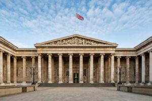 The British Museum - London - Außenansicht: Der imposante, klassizistische Haupteingang des Museums mit der großen Säulenreihe, dem skulptierten Giebel und wehender britischer Flagge