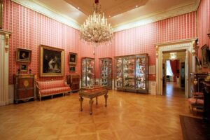 The Wallace Collection - London - Arbeitszimmer: Ein Raum mit rot-weiß gestreiften Tapeten, opulenten Kristallkronleuchtern und Vitrinen voller wertvollem Porzellan und Silber