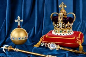 Tower of London - Ausstellung: Die britischen Kronjuwelen mit der St. Edward’s Krone, dem Reichsapfel in matter Gold-Optik und dem Zepter auf blauem Samt.