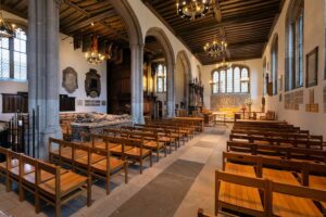 Tower of London - Kapelle St. Peter ad Vincula: Blick in den Kirchenraum mit hölzernen Kirchenbänken, Steinsäulen und einem historischen Grabmonument im Vordergrund