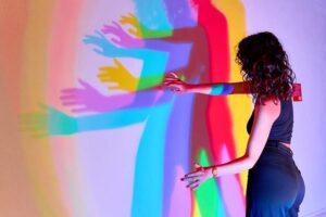 WOW Museum - München - Licht und Schatten Illusion: Eine Person erzeugt bunte, mehrfache Schatten an einer beleuchteten Wand